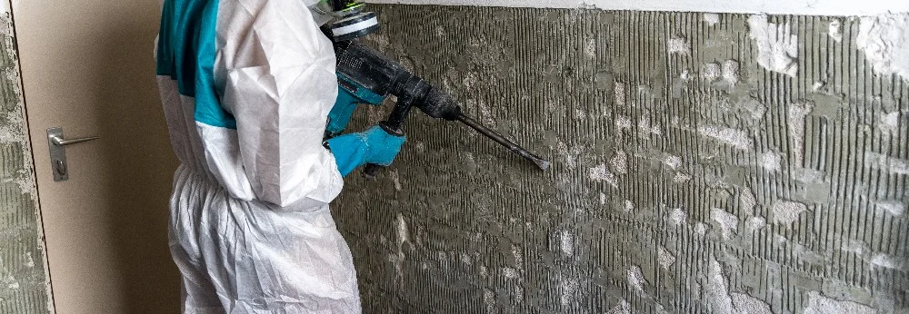 Person in Schutzkleidung entfernt Fliesenkleber mit Bohrhammer.